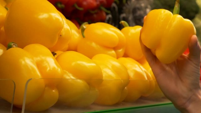 Young guy chooses yellow bell pepper in the supermarket. Hand takes yellow pepper from the counter in the store. Healthy food. 4K footage