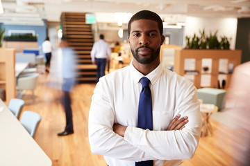 Portrait Of Businessman In Busy Modern Office With Blurred Colleagues Working In Background