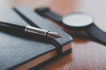 A fountain pen on a notebook near a watch