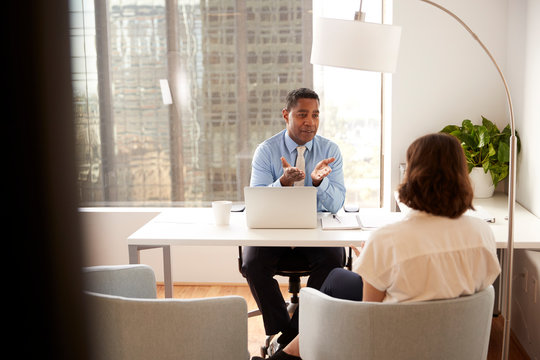 Male Financial Advisor In Modern Office Sitting At Desk Meeting Female Client