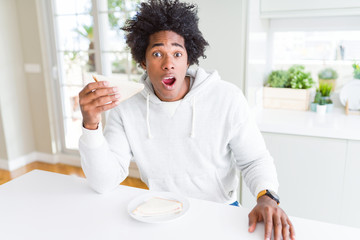 Fototapeta na wymiar African American man eating handmade sandwich at home scared in shock with a surprise face, afraid and excited with fear expression