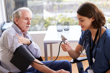 Nurse Wearing Scrubs In Office Checking Senior Male Patients Blood Pressure