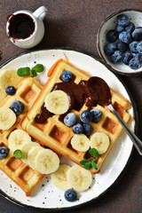 Breakfast time. Homemade waffles with banana, blueberry and chocolate spread on a kitchen table.