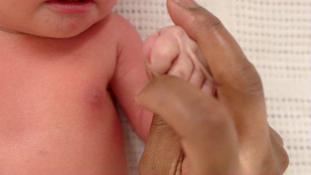 Mother moisturizing and massages her newborn baby's hand.