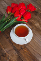 Spring flowers. Bouquet of Red tulips with tea cup on brown wooden background. Mother's Day and Valentines Day concept.