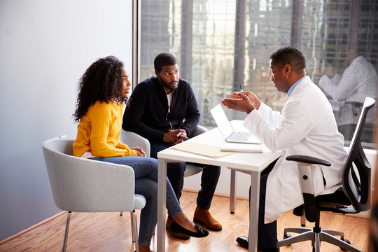 Couple Having Consultation With Male Doctor In Hospital Office