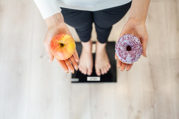 Diet. Woman Measuring Body Weight On Weighing Scale Holding Donut and apple. Sweets Are Unhealthy...