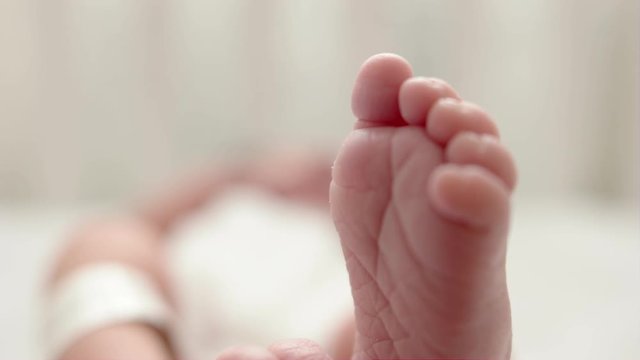 Newborn baby lying in cot. Baby is kicking and stretching legs. Closeup detail on soles of feet. Baby sweetly bends her big toe and touches her feet together.