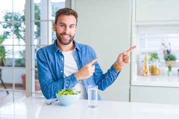 Handsome man eating fresh healthy salad smiling and looking at the camera pointing with two hands and fingers to the side.