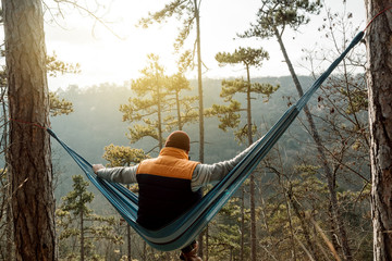 Young happy man relaxing lying in hammock on top of mountain.