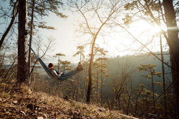 Young happy man relaxing lying in hammock on top of mountain.