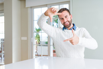 Fototapeta premium Handsome man wearing casual sweater smiling making frame with hands and fingers with happy face. Creativity and photography concept.