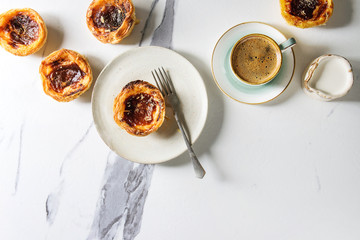 Traditional Portuguese egg tart dessert Pasteis Pastel de nata with cup of black coffee and jug of milk over white marble background. Flat lay, space