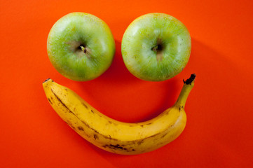 Banana and two apples lying in the shape of a smiley on a bright orange background