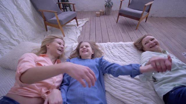 happy family, funny sisters with mom fall on bed during fun laugh and tickle little girl at home
