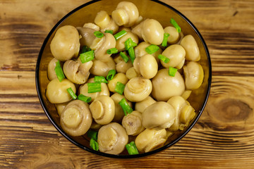 Glass bowl with pickled champignons. Marinated mushrooms on wooden table