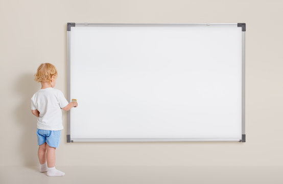 Little boy with paint brush standing near blank whiteboard