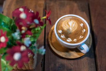 Latte art coffee cup on wooden table with flowers pot