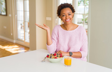 Young african american woman having healthy breakfast in the morning at home smiling cheerful presenting and pointing with palm of hand looking at the camera.