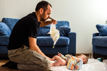 Novice father changing the stinking diaper of a baby with a gesture of disgust. - obrazy, fototapety, plakaty