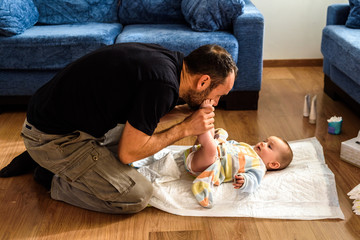 Father changing his daughter's dirty diaper on the living room floor.