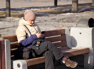 Russia, Krasnoyarsk, February 2019: The girl on the bench looking at the phone.