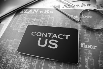 Business accessories, design and construction projects, blueprints, drawings on the desktop with tablet with text Contact us