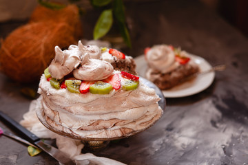 ropical aquafaba cake with kiwi, strawberry and coconut cream on dark table with ingredients and flowers
