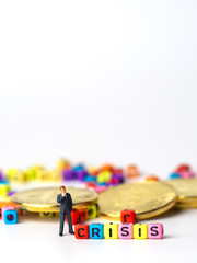 miniature figure businessman in dark blue suit standing backside of colorful of CRISIS alphabet and golden coin and thinking of the crisis will come.
