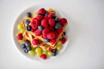 Sweet toddler birthday boy, eating belgian waffle with raspberries, blueberries, cocnut and chocolate
