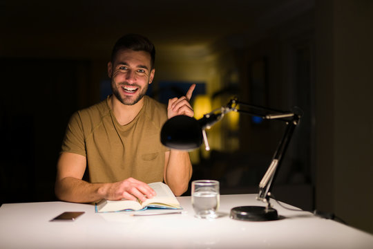 Young handsome student man studying at night at home very happy pointing with hand and finger to the side