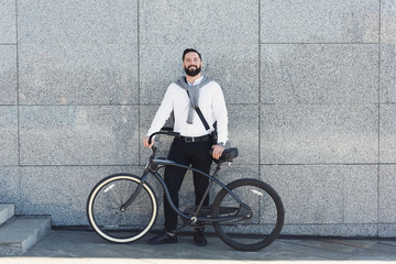 Fototapeta premium Businessman standing against building wall with his bicycle.