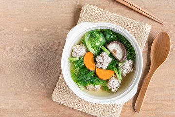 top view of lettuce clear soup with pork balls in a ceramic bowl on wooden table. asian homemade style food concept.