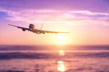 Fototapeta na wymiar Airplane flying over blur tropical beach with smooth wave and sunset sky abstract background.
