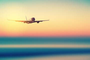 Airplane flying over blur tropical beach with smooth wave and sunset sky abstract background.
