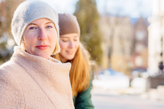 Mature blonde mother and her aduld daughter walking outoor in beautiful frosty sunny winter day. Bonding, different generationsconnect, family concept.