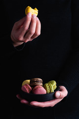 verschiedene Macarons mit unterschiedlichen Geschmacksrichtungen in dunkler Keramikschale von Hand...