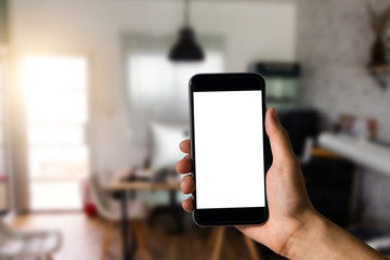 Hand holding white mobile phone with blank white screen  in office.