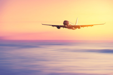Airplane flying over blur tropical beach with smooth wave and sunset sky abstract background.