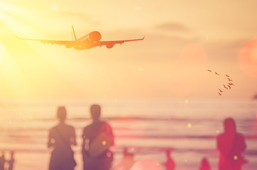 Fototapeta premium Airplane flying over blur people relax on tropical sunset beach with bokeh sun light and birds abstract background.