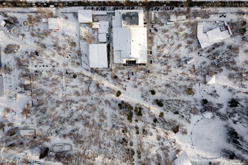 Aerial top view from above of a park with trees and buildings covered with white snow in the center of the city near a highway with cars on a winter sunny day