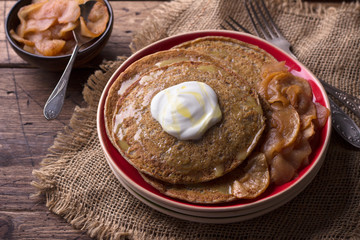 Vegetarian buckwheat pancakes with baked apples with cinnamon, honey and fresh cream on a wooden table