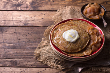 Fototapeta na wymiar Vegetarian buckwheat pancakes with baked apples with cinnamon, honey and fresh cream on a wooden table