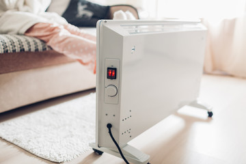 Using heater at home in winter. Woman warming her feet. Heating season.