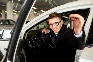 Salesman smiling holds car keys in car.