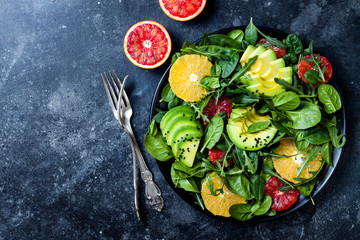 Citrus salad with mixed greens and blood orange on black ceramic plate. Vegan, vegetarian, clean eating, dieting, food concept. Dark stone background.