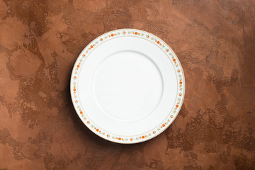 White plate with ornament empty brown background. Isolated item pattern. Copy space space for design. View from above.