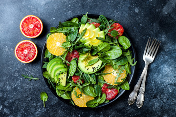 Citrus salad with mixed greens and blood orange on black ceramic plate. Vegan, vegetarian, clean eating, dieting, food concept. Dark stone background.