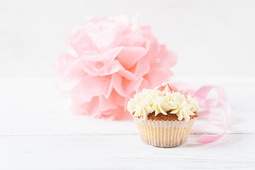Muffin is decorated with thick white and pink cream on a light background. Festive food concept. Selective focus.