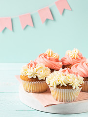 Muffins are decorated with thick white and pink cream light blue background pink festive flags. Festive food concept.